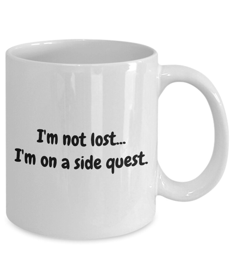 May include: White ceramic coffee mug with black text that reads "I'm not lost... I'm on a side quest."