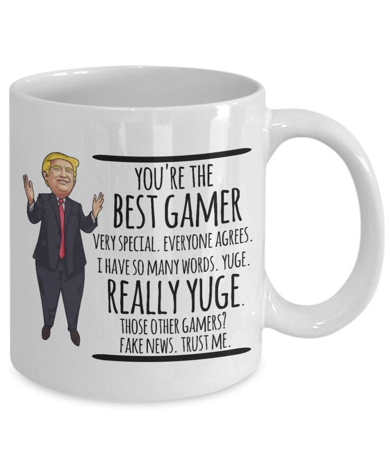 May include: White ceramic coffee mug with a cartoon image of a man in a suit and red tie. The text on the mug reads "You're the Best Gamer Very Special. Everyone Agrees. I have so many words. YUGE. REALLY YUGE. Those other gamers? Fake news. Trust me."