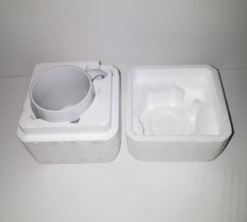 K&ouml;nnte beinhalten: Eine wei&szlig;e Keramiktasse mit Henkel, verpackt in einem wei&szlig;en Styropor-Karton mit einem separaten Styropor-Einsatz f&uuml;r die Tasse.