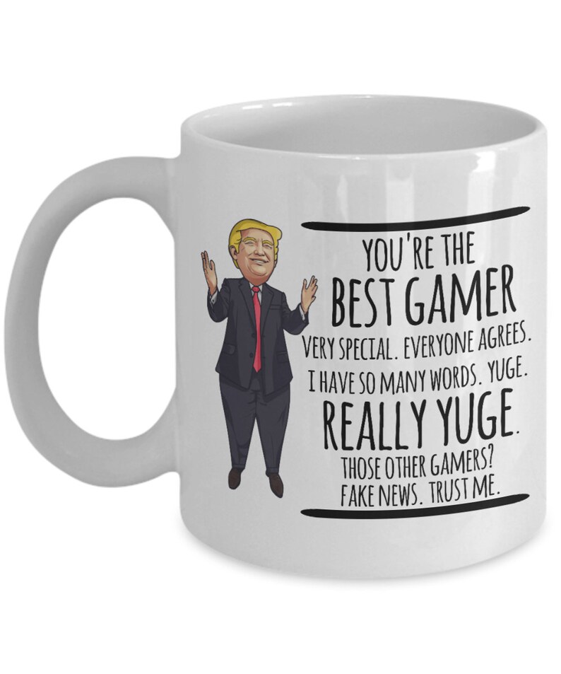 May include: White ceramic coffee mug with a cartoon image of a man in a suit and red tie. The text on the mug reads "You're the Best Gamer. Very special. Everyone agrees. I have so many words. Yuge. Really Yuge. Those other gamers? Fake news. Trust me."