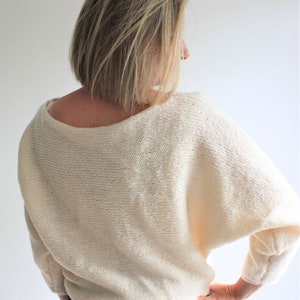 Könnte beinhalten: Ein weißer Strickpullover mit lockerer Passform und einem weiten Ausschnitt. Der Pullover ist aus einem weichen, leichten Garn gefertigt.