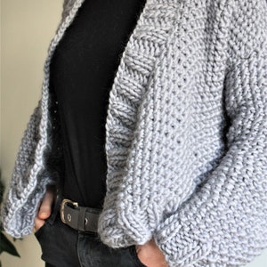 May include: A gray knitted cardigan with a loose fit and long sleeves. The cardigan is open in the front and has a simple design.