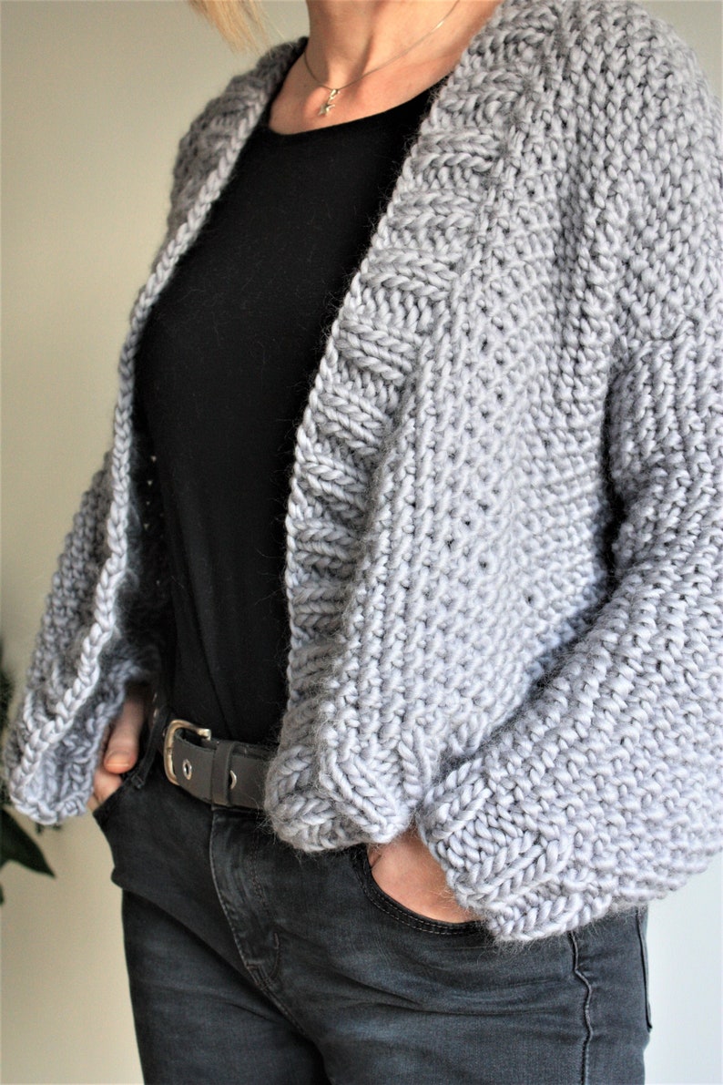 May include: A gray knitted cardigan with a loose fit and long sleeves. The cardigan is open in the front and has a simple design.