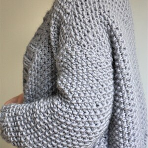 May include: A gray knitted sweater with a loose fit and long sleeves.
