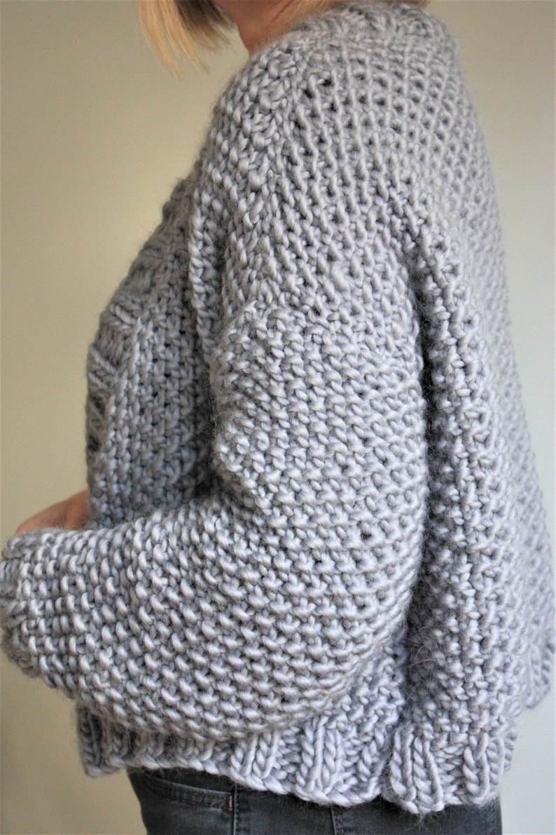May include: A gray knitted sweater with a loose fit and long sleeves.