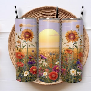 May include: Three stainless steel tumblers with a floral design featuring sunflowers and wildflowers. The design includes a sunset scene with a yellow sun and a field of wheat. Each tumbler has a black straw.