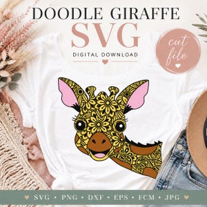 Op de afbeelding: Een wit t-shirt met een afbeelding van een giraffekop met een geel en zwart bloemrijk doodle-patroon, roze binnenoren en een bruine snuit. De tekst luidt DOODLE GIRAFFE SVG DIGITAL DOWNLOAD en cut file.