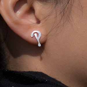 Puede incluir: Pendientes de plata con un diseño abstracto único. Los pendientes tienen forma de signo de interrogación con una gota en la parte inferior.