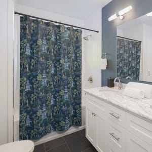 May include: A dark blue shower curtain with a repeating pattern of Asian-inspired pagodas, trees, and landscapes in shades of green, blue, and beige. The curtain is hanging in a bathroom with white fixtures and a marble countertop.