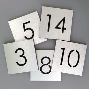 May include: Six silver metal square table number signs with black numbers. The numbers are 3, 5, 8, 10, 14.