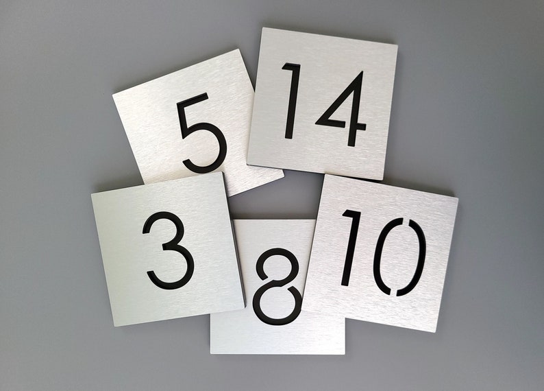 May include: Six silver metal square table number signs with black numbers. The numbers are 3, 5, 8, 10, 14.