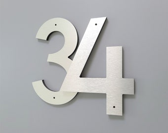 May include: Silver metal house numbers 34, with a modern, contemporary design. The numbers are attached to a wall.
