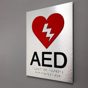 ADA AED sign. Fire emergency ADA compliant signs. Automated external defibrillator sign with red pictogram and Grade 2 Braille.