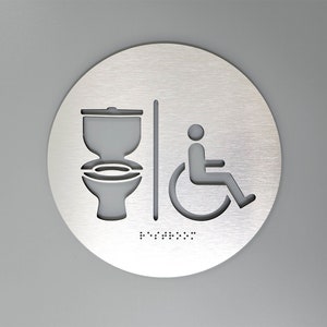 May include: A round, silver-colored sign with a toilet and wheelchair symbol. The sign also includes braille text.