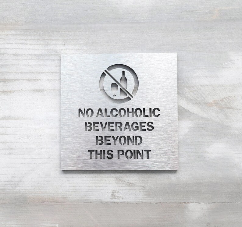 May include: A silver metal sign with a no alcoholic beverages symbol and the text "NO ALCOHOLIC BEVERAGES BEYOND THIS POINT".