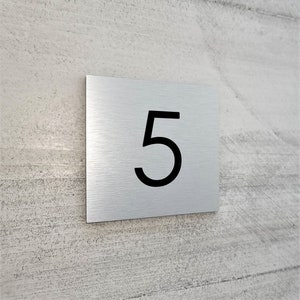 May include: A brushed silver metal house number plaque with the number 5 printed in black.