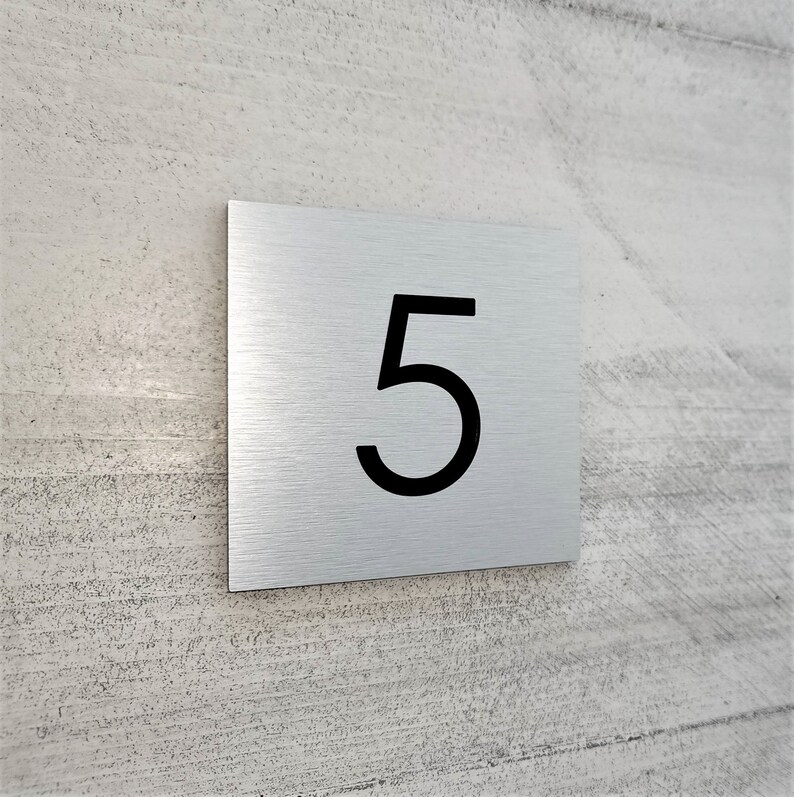 May include: A brushed silver metal house number plaque with the number 5 printed in black.
