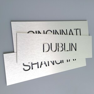 May include: Three silver metal plaques with the words "Cincinnati", "Dublin", and "Shanghai" cut out of the metal.