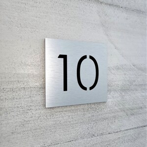 May include: A silver metal house number plaque with the number 10 cut out in black.