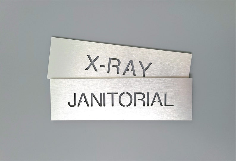 May include: Two silver metal signs with cut-out lettering. The top sign says "X-RAY" and the bottom sign says "JANITORIAL".