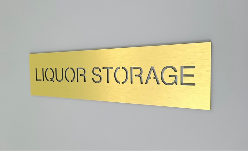 May include: A gold metal sign with the words "LIQUOR STORAGE" cut out.