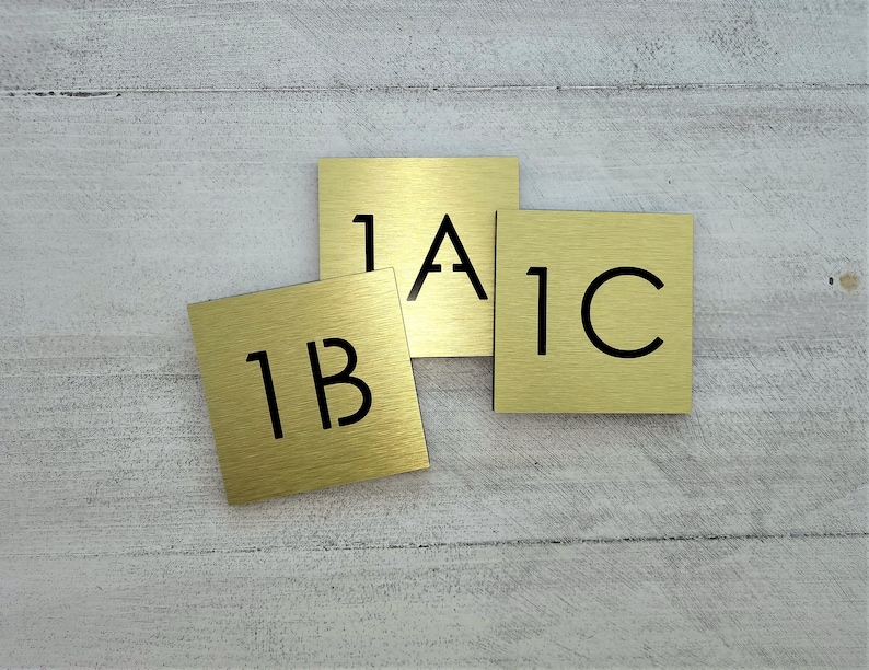 May include: Three gold-colored metal plaques with black lettering. The plaques are labeled "1A", "1B", and "1C".