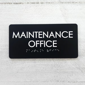 K&ouml;nnte beinhalten: Schwarzes Schild mit wei&szlig;em Text, auf dem "MAINTENANCE OFFICE" steht, mit Braille darunter.