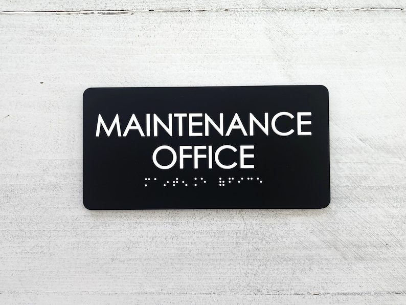 K&ouml;nnte beinhalten: Schwarzes Schild mit wei&szlig;em Text, auf dem "MAINTENANCE OFFICE" steht, mit Braille darunter.