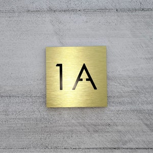 May include: A gold metal square sign with the number "1A" printed in black.