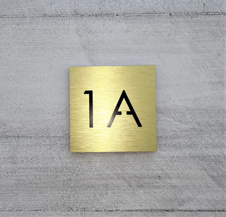 May include: A gold metal square sign with the number "1A" printed in black.