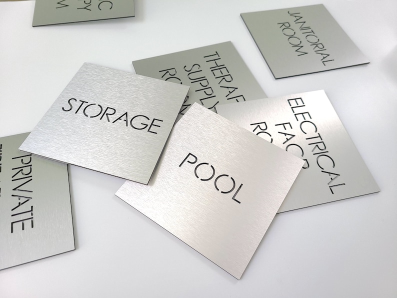 May include: A collection of square, brushed metal signs with black text. The signs are labeled with various room names, including "STORAGE," "POOL," and "ELECTRICAL FACILITY ROOM."