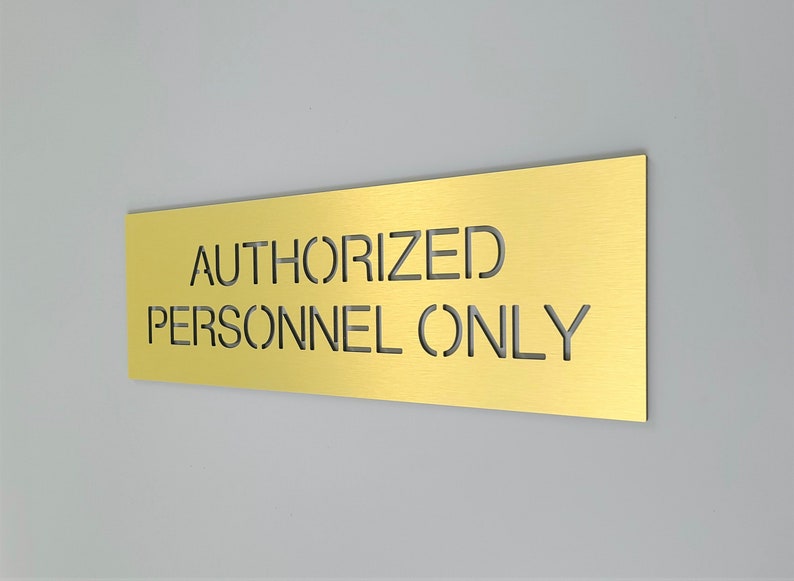 May include: A gold metal sign with the text "AUTHORIZED PERSONNEL ONLY" cut out of the metal.