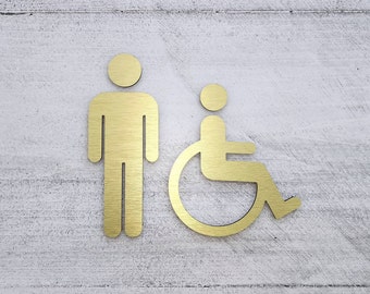 Könnte beinhalten: Goldfarbenes Metallschild mit zwei Figuren. Die Figur links ist eine stehende Person. Die Figur rechts ist eine Person, die in einem Rollstuhl sitzt.