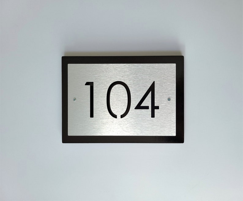 May include: A black framed silver plaque with the number 104 printed in black.