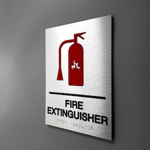 May include: A silver metal sign with a red fire extinguisher icon and the text "FIRE EXTINGUISHER" in black. The sign also includes braille text.