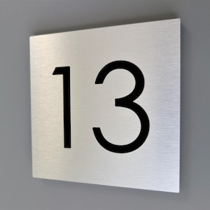 May include: A brushed silver metal sign with the number 13 printed in black.