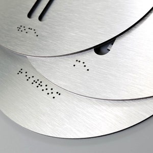 May include: Three silver metal discs with braille lettering. The top disc has the braille letters "B" and "T". The middle disc has the braille letter "T". The bottom disc has the braille letters "A" and "U" followed by the braille letters "T" and "O".