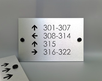 May include: A silver metal sign with black arrows and room numbers. The sign reads: 301-307, 308-314, 315, 316-322.