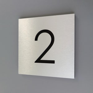 May include: A brushed silver metal house number sign with the number 2 in black.