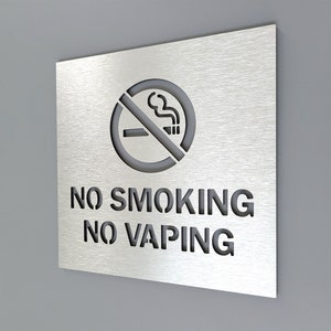 Könnte beinhalten: Ein silbernes Metallschild mit einem Nichtraucher-Symbol und dem Text "NO SMOKING NO VAPING".