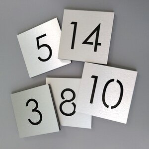 May include: Five silver metal squares with black numbers on them. The numbers are 3, 5, 8, 10, and 14.