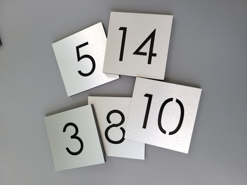 May include: Five silver metal squares with black numbers on them. The numbers are 3, 5, 8, 10, and 14.