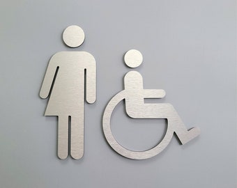 Könnte beinhalten: Ein silbernes Metallschild mit zwei Symbolen. Das erste Symbol ist eine Person mit einem Rock. Das zweite Symbol ist eine Person im Rollstuhl.