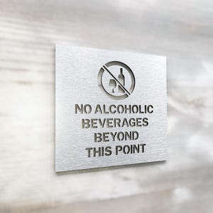 May include: A silver metal sign with a no alcohol symbol and the text "NO ALCOHOLIC BEVERAGES BEYOND THIS POINT".