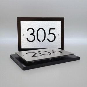 May include: Two silver metal house number plaques with black numbers. The top plaque has the number 305 and the bottom plaque has the number 206.