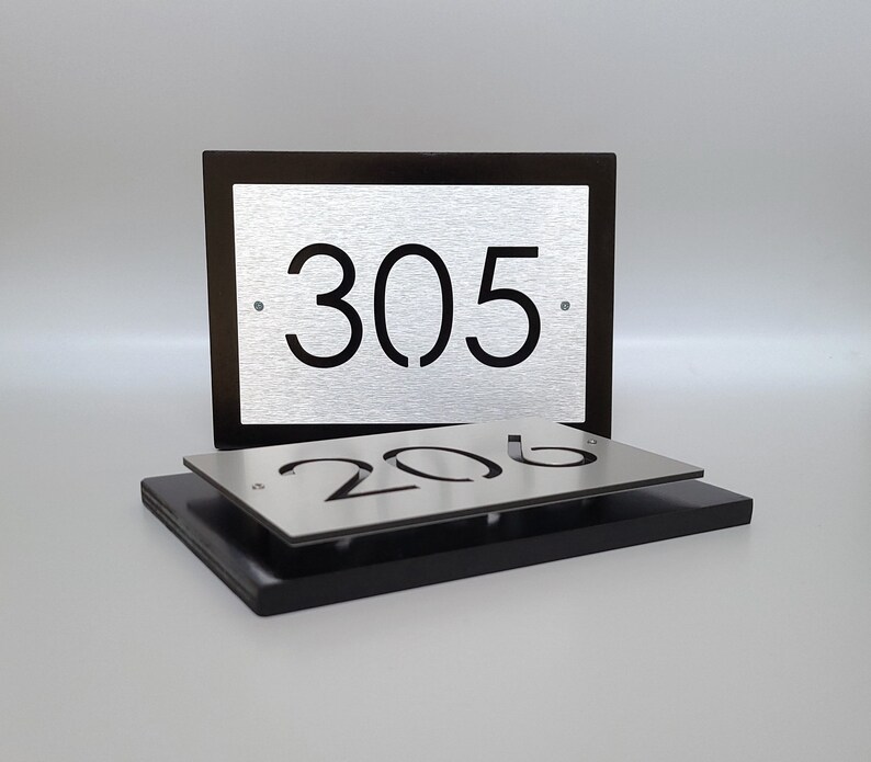 May include: Two silver metal house number plaques with black numbers. The top plaque has the number 305 and the bottom plaque has the number 206.