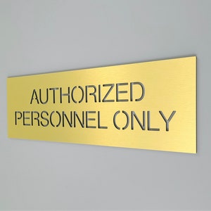Può includere: Un cartello in metallo dorato con il testo "AUTHORIZED PERSONNEL ONLY" tagliato nel metallo.