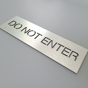 May include: A brushed silver metal sign with the text "DO NOT ENTER" cut out in black.