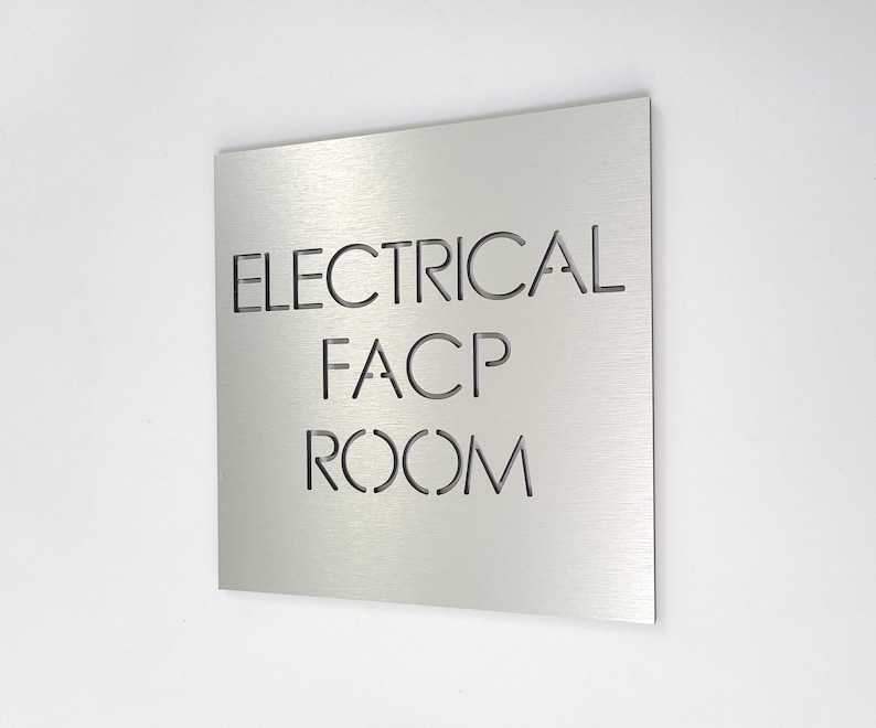 May include: A square, brushed metal sign with the words "ELECTRICAL FACP ROOM" cut out. The sign is mounted on a white wall. The letters are in a sans-serif font.