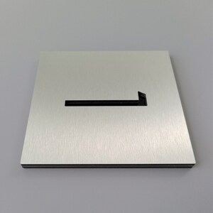 May include: A brushed silver metal sign with a cut-out arrow pointing to the left. The sign is rectangular and has a black border.